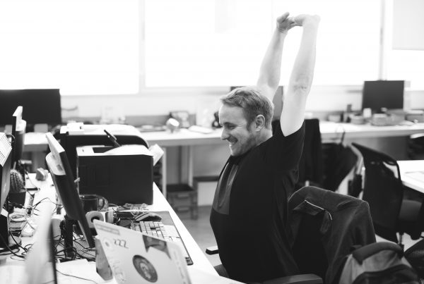 black and white image of a man at his desk at work smiling and doing exercise at work