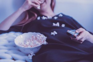 woman eating pop corn and watching TV for a blog by Wellsace on Absenteeism vs presenteeism