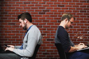 two men sittingback to back at work, representing blog by Wellspace on 7 signs you have an unhappy employee