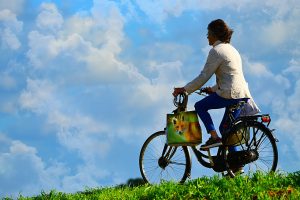 woman riding a bike throug a meadow to illustrate blog by Wellspace on the three pillar of health: activity