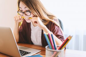 woman biting pencil and looking at laptop for national Stress Awareness Week