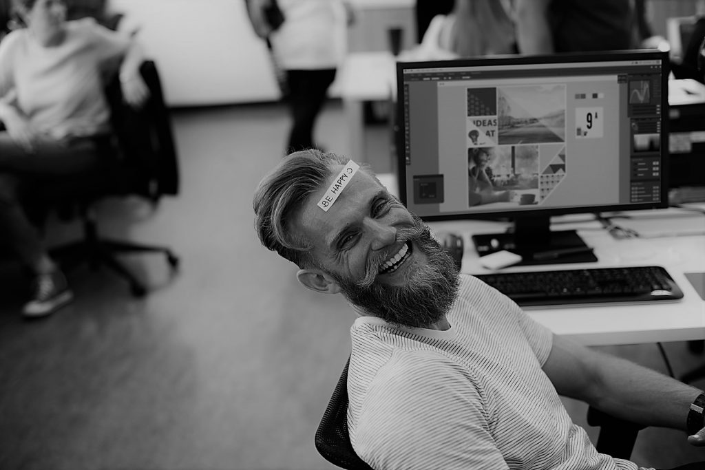 image shows an office worker with a sticker on his head that says be happy