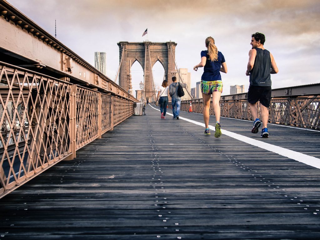 Man and woman jogging along a bridge with people walking in distance for Wellspace blog Looking After Your Workplace Wellbeing