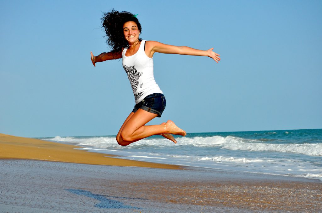 healthy woman jumping on a beach for workplace wellness blog for Wellspace on is workplace wellness important