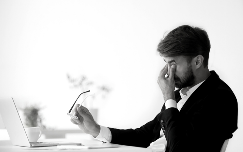 A man lacking energy holding his eyes in front of his work laptop, black and white effect