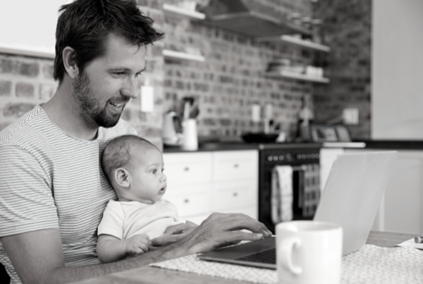 A man with a baby on his lap working from home in his kitchen