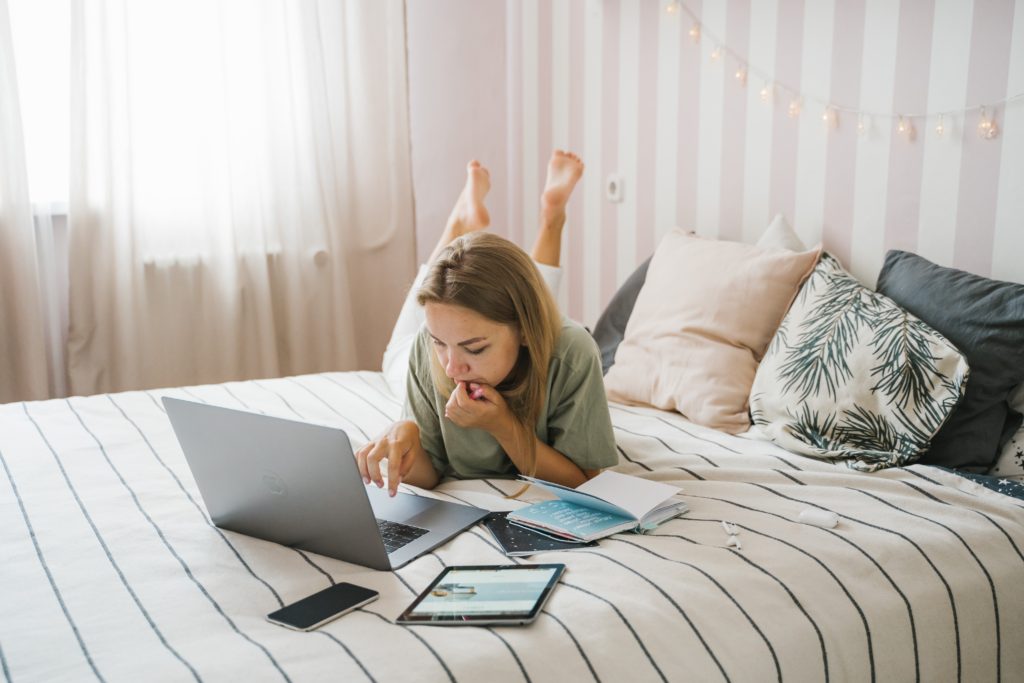 working from home woman lying on bed with a laptop