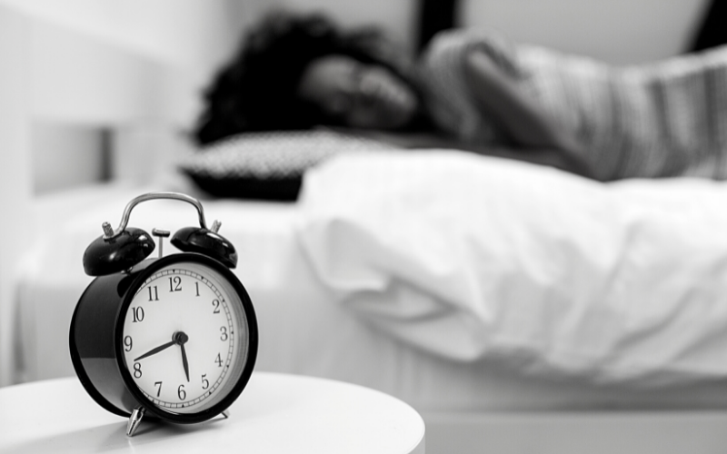Image of a person sleeping next to an alarm clock for blog by Wellspace on improving sleep