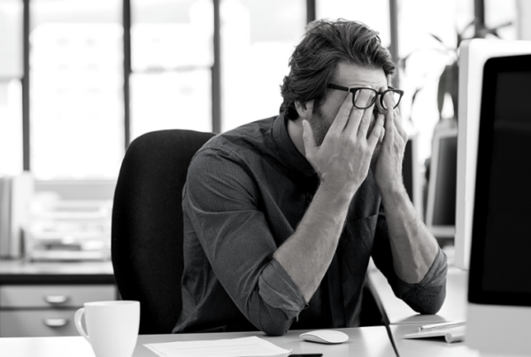 Man with glasses on looking stressed at his computer